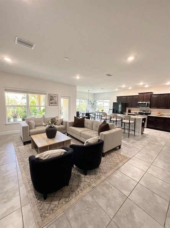 An open-concept living room and kitchen feature tile flooring, dark cabinetry, and neutral furniture — 13058 OGDEN GLADE ROAD, DADE CITY, FL