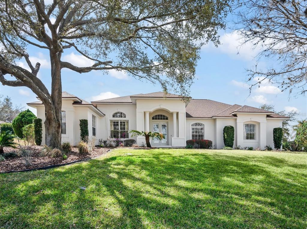 A single-story stucco house with a large tree in the front yard — 39407 TREELINE DRIVE, LADY LAKE, FL