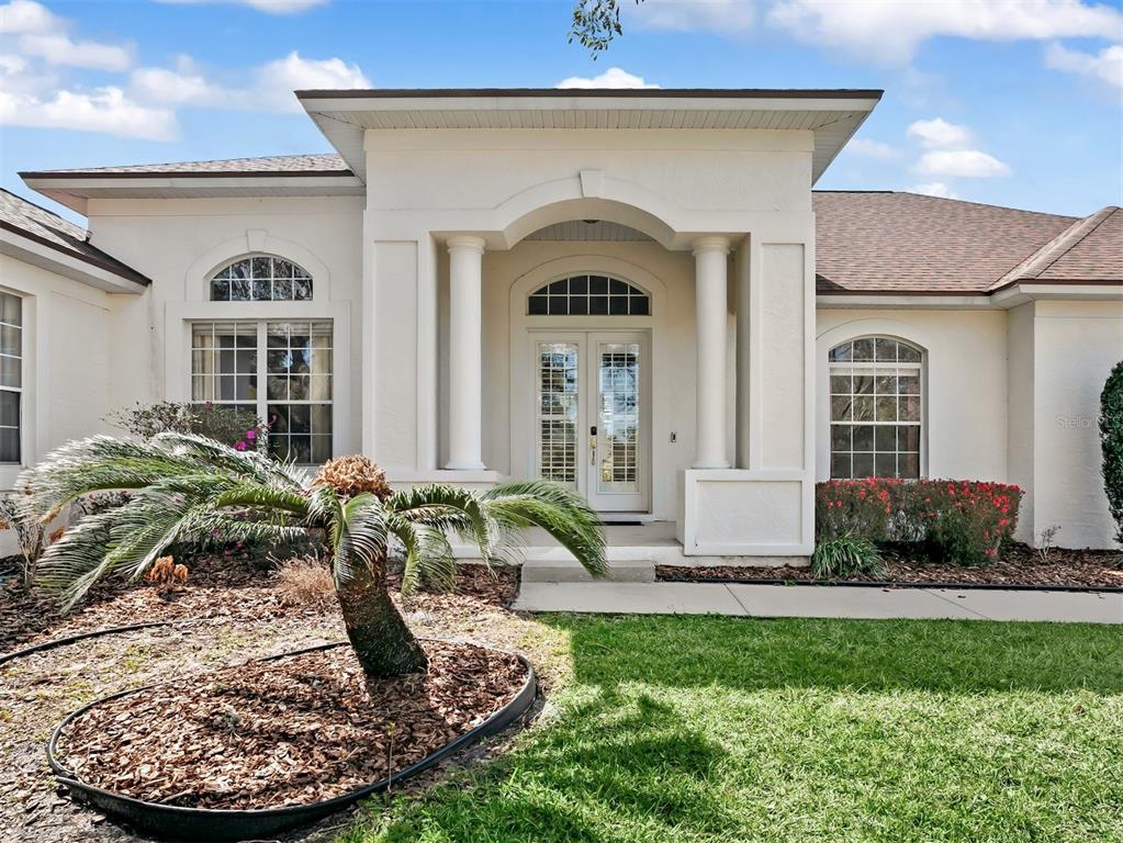 The exterior of a single-story house features a covered entryway with columns and double doors — 39407 TREELINE DRIVE, LADY LAKE, FL