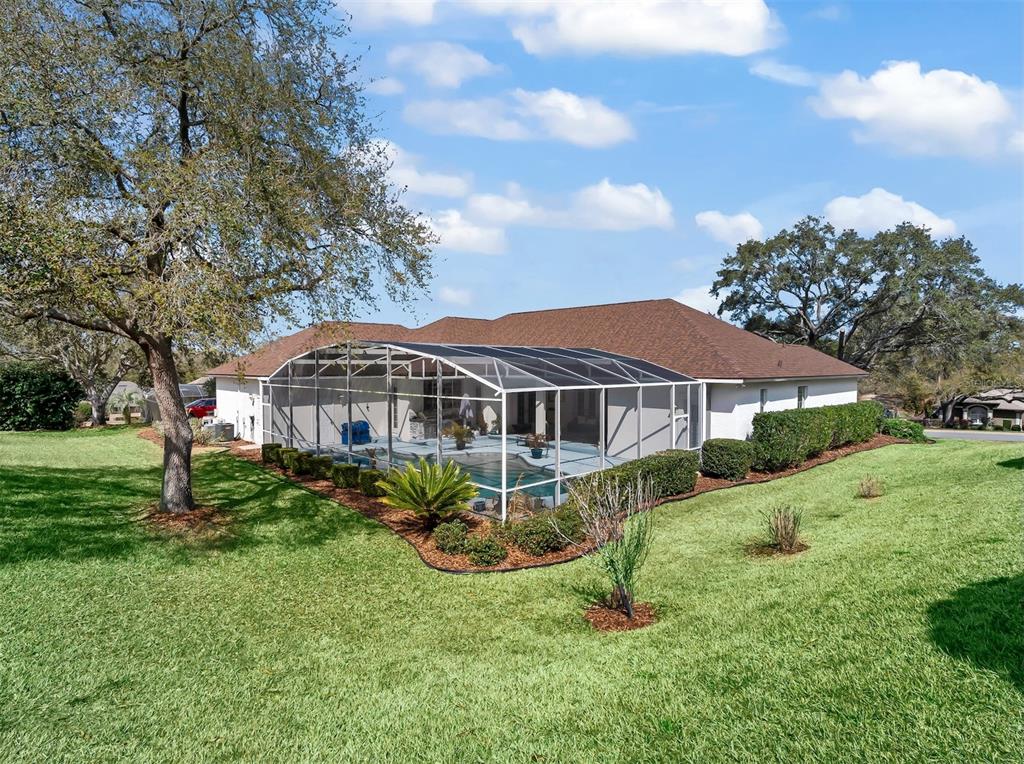 A backyard view of a house with a screened-in pool enclosure and large oak trees — 39407 TREELINE DRIVE, LADY LAKE, FL
