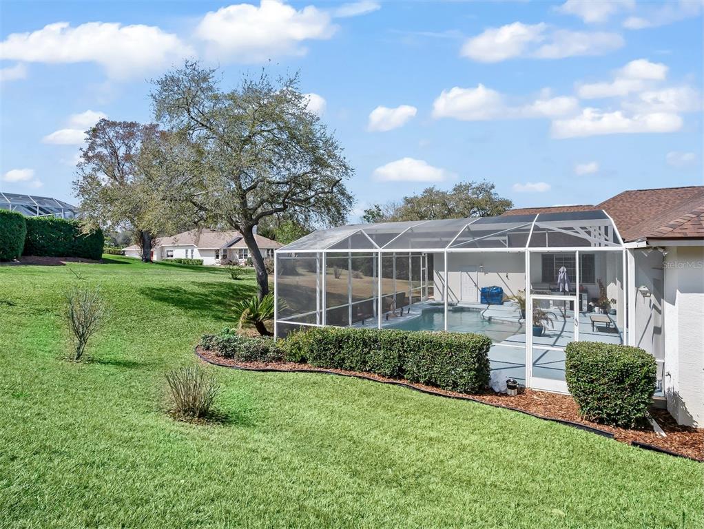 A screened-in swimming pool sits in the backyard of a house with a grassy lawn — 39407 TREELINE DRIVE, LADY LAKE, FL