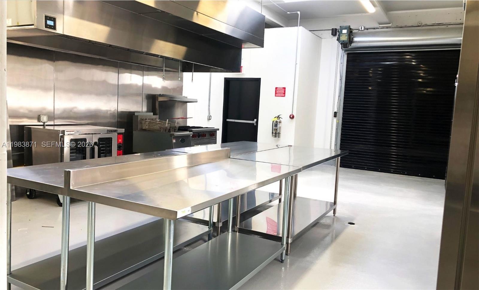 A commercial kitchen features stainless steel prep tables, cooking equipment, and a large roll-up door — 7700 NW 7th Ave, Miami FL 33150, MIAMI, FL