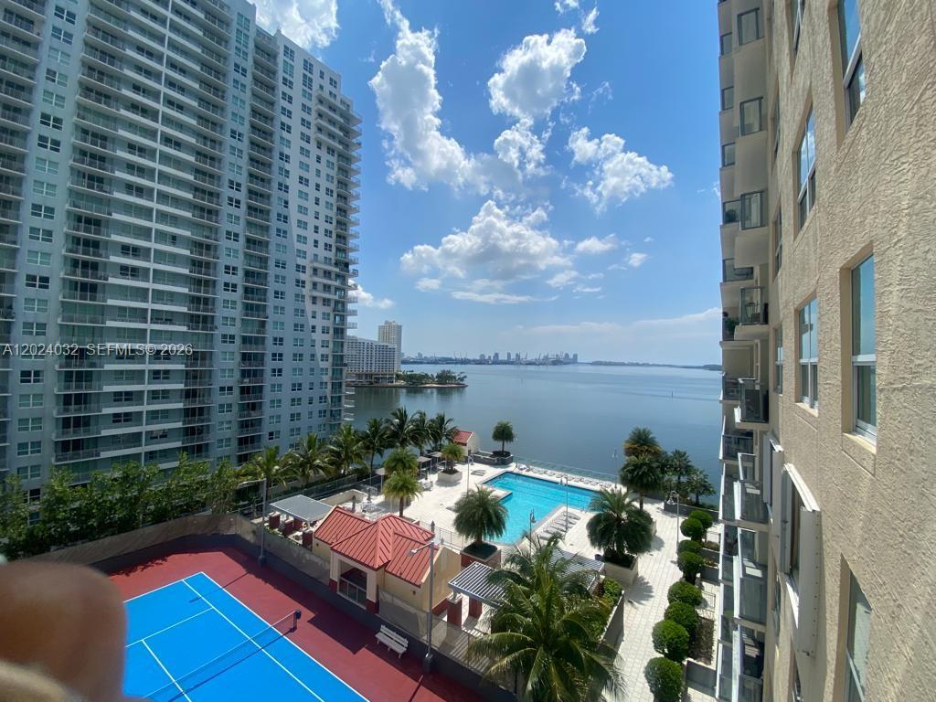 An elevated view of a tennis court, swimming pool, and bay from a balcony — 1155 Brickell Bay Dr # 1202, Miami FL 33131, MIAMI, FL