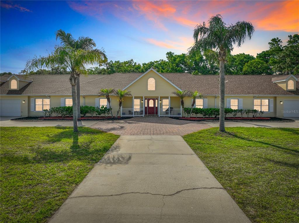 A yellow, single-story house with a paved driveway, palm trees, and a central front entrance — 2300 PINE MEADOWS PLACE, CHULUOTA, FL