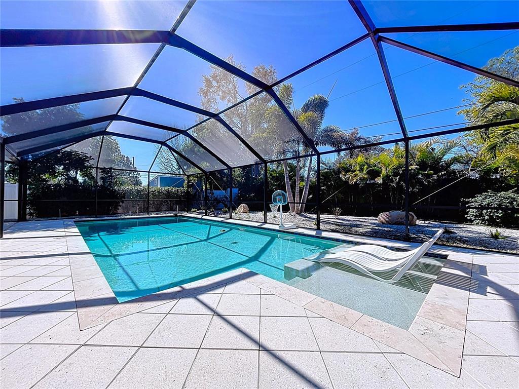 A swimming pool with a tanning ledge and lounge chairs sits inside a screened enclosure — 1468 S PRESCOTT AVENUE, CLEARWATER, FL