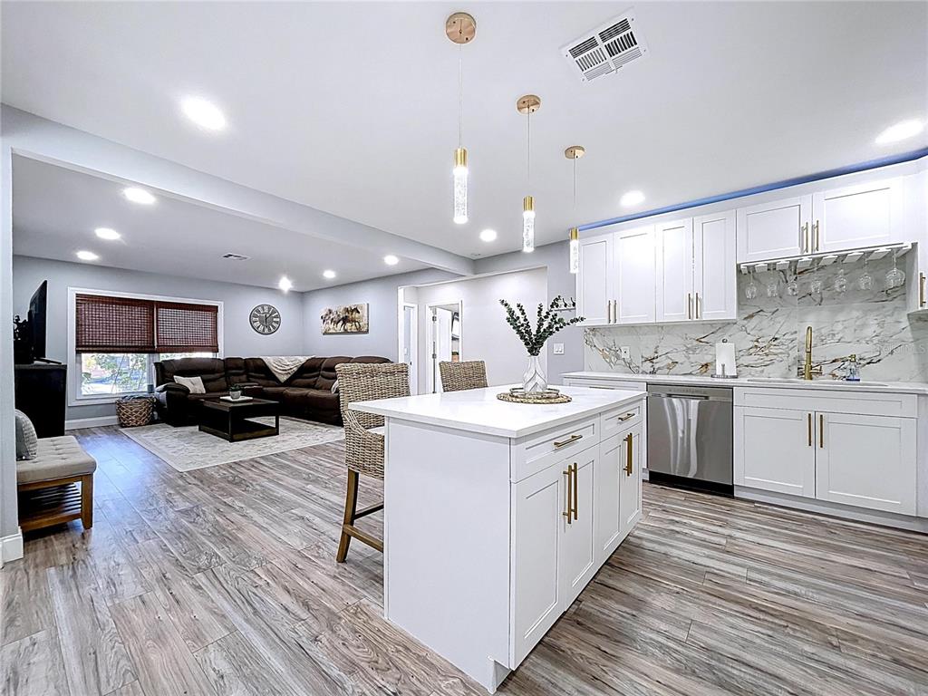 A modern kitchen with white cabinets, gold hardware, and a central island overlooks a living room — 1468 S PRESCOTT AVENUE, CLEARWATER, FL