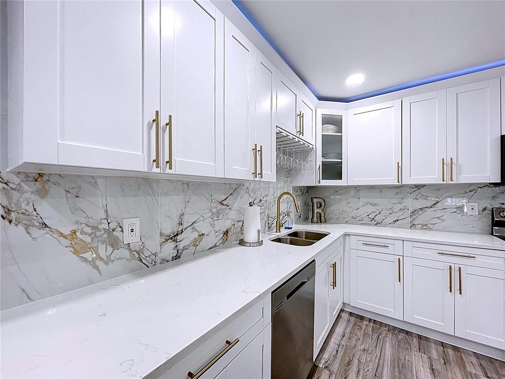 A kitchen features white shaker cabinets, gold hardware, marble-patterned backsplash, and light-colored countertops — 1468 S PRESCOTT AVENUE, CLEARWATER, FL