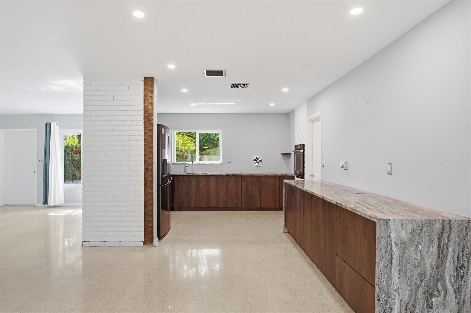 A kitchen features dark wood cabinets, stone countertops, a white brick pillar, and light flooring — 370 SW 13th Street, Pompano Beach FL 33060, POMPANO BEACH, FL