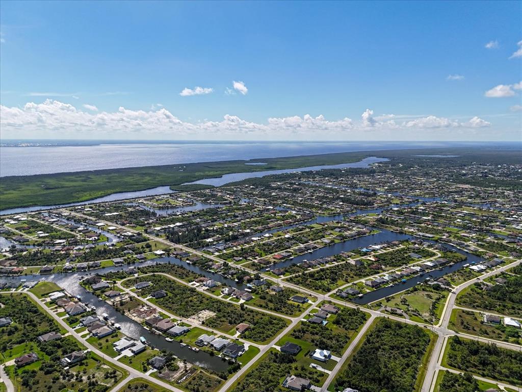 An aerial view shows a residential neighborhood with canals leading to a large body of water — 8295 ANTWERP CIRCLE, PORT CHARLOTTE, FL