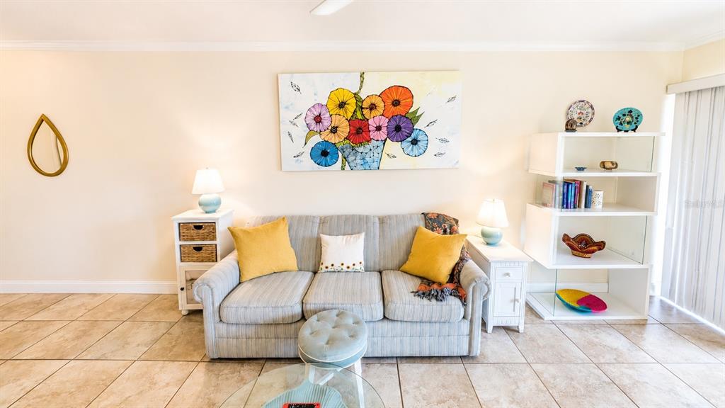 A living room features a striped sofa, yellow throw pillows, wall art, and white shelving — 3413 CLARK ROAD UNIT 114, SARASOTA, FL