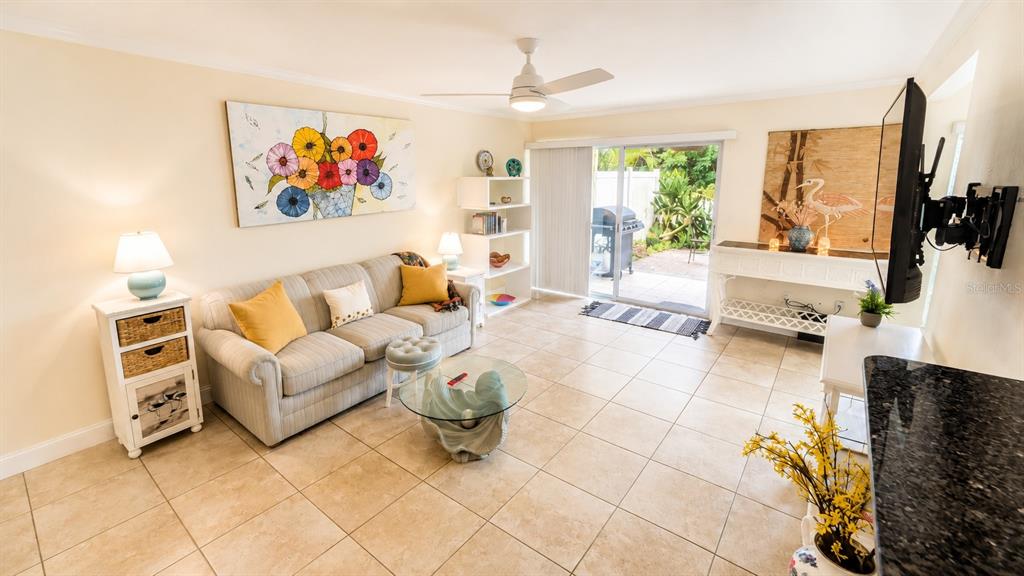 A living room features a beige sofa, tile flooring, a ceiling fan, and a sliding door — 3413 CLARK ROAD UNIT 114, SARASOTA, FL
