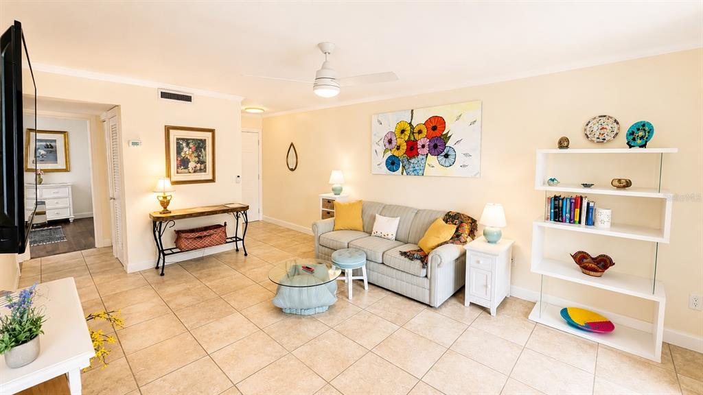 A living room features a beige sofa, tiled floors, a white bookshelf, and wall art — 3413 CLARK ROAD UNIT 114, SARASOTA, FL