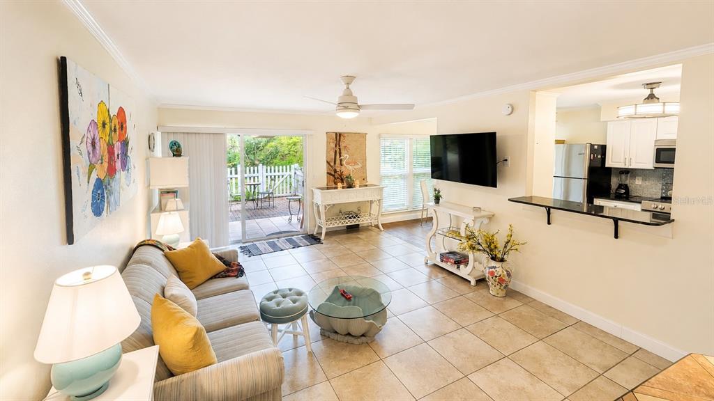 A living room with tile floors, a sofa, a wall-mounted television, and a kitchen pass-through — 3413 CLARK ROAD UNIT 114, SARASOTA, FL