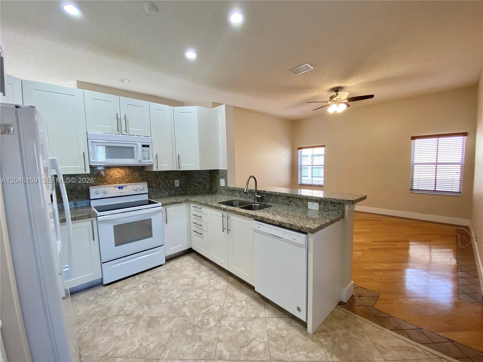 A kitchen with white cabinets, granite countertops, and tile flooring opens to a living area — 837 Tanglewood Cir, Weston FL 33327, WESTON, FL