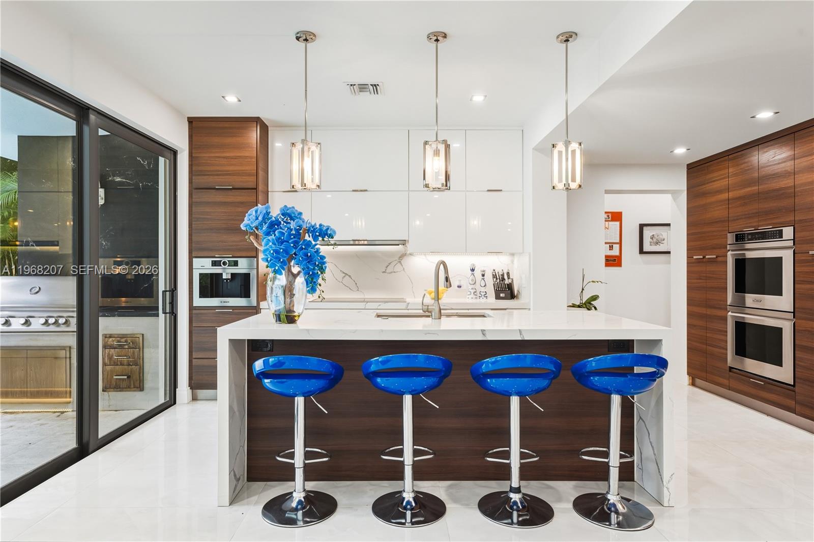 A modern kitchen features a white marble island with four blue stools and wood cabinetry — 400 NW 24th St, Wilton Manors FL 33311, WILTON MANORS, FL