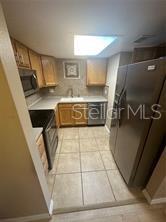 A kitchen features light wood cabinets, stainless steel appliances, and beige tile flooring — 904 LAKE DESTINY ROAD UNIT H, ALTAMONTE SPRINGS, FL