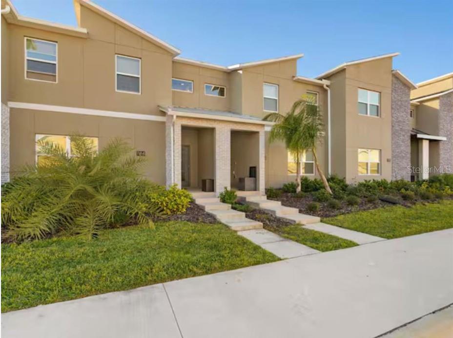 A two-story townhouse exterior with tan stucco walls, a palm tree, and concrete walkways — 1184 KINGSBARN STREET, DAVENPORT, FL