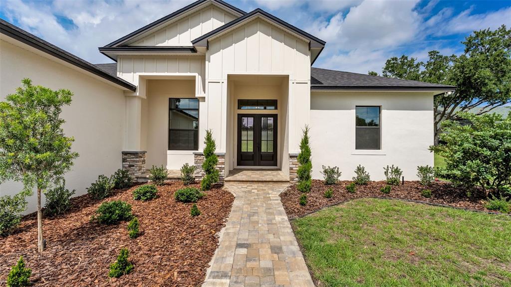 A modern single-story house features a stone-accented entryway, dark double doors, and landscaped mulch beds — 6827 LAKELAND HIGHLANDS ROAD, LAKELAND, FL
