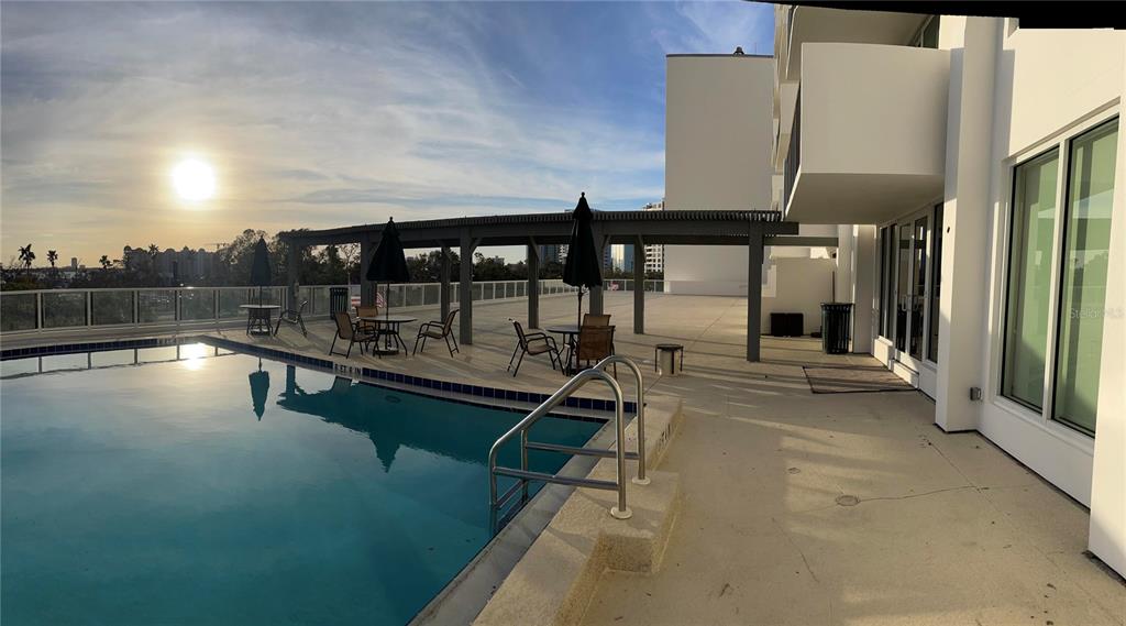 A swimming pool with a metal ladder sits on a patio with tables and umbrellas — 101 S GULFSTREAM AVENUE UNIT 10B, SARASOTA, FL