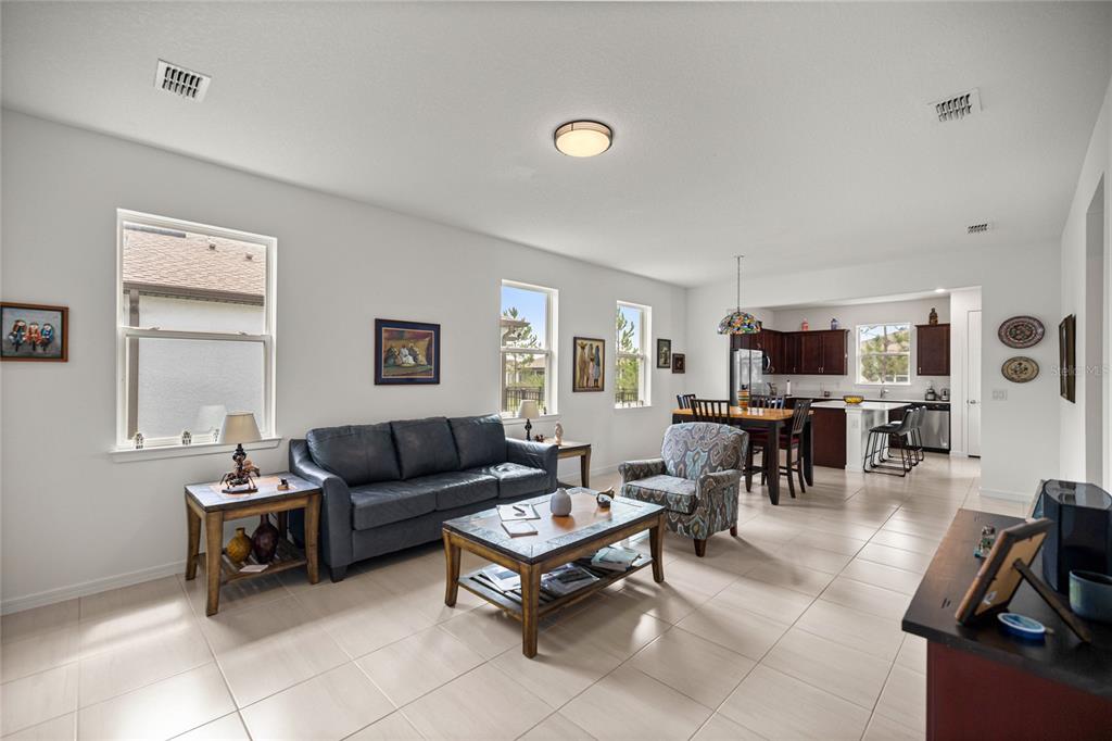 An open-concept living room and kitchen with tile flooring, a dark sofa, and dining area — 9412 SW 53RD PLACE, OCALA, FL