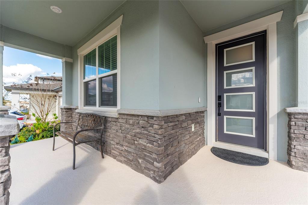 A covered front porch features a dark door with glass panels and stone veneer siding — 2284 BEAR PEAK ROAD, CLERMONT, FL