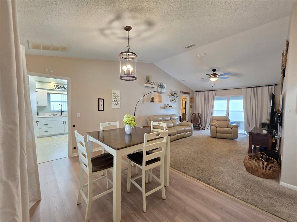 An open-concept living and dining area features light wood flooring, carpet, and a vaulted ceiling — 2258 SILVER RE DRIVE, LAKELAND, FL