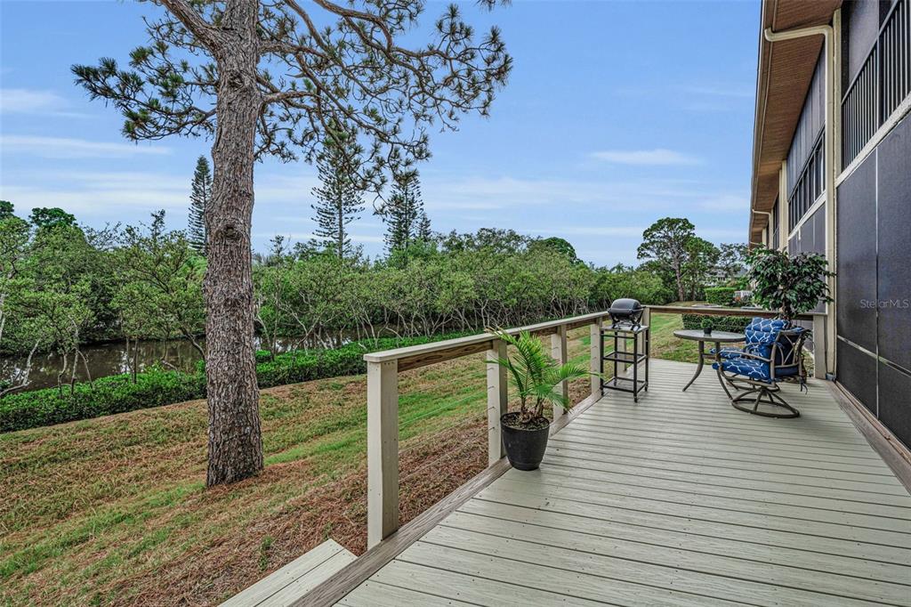 A wooden deck overlooks a grassy yard, a small canal, and a line of trees — 1673 SEASCAPE CIRCLE UNIT 102, TARPON SPRINGS, FL