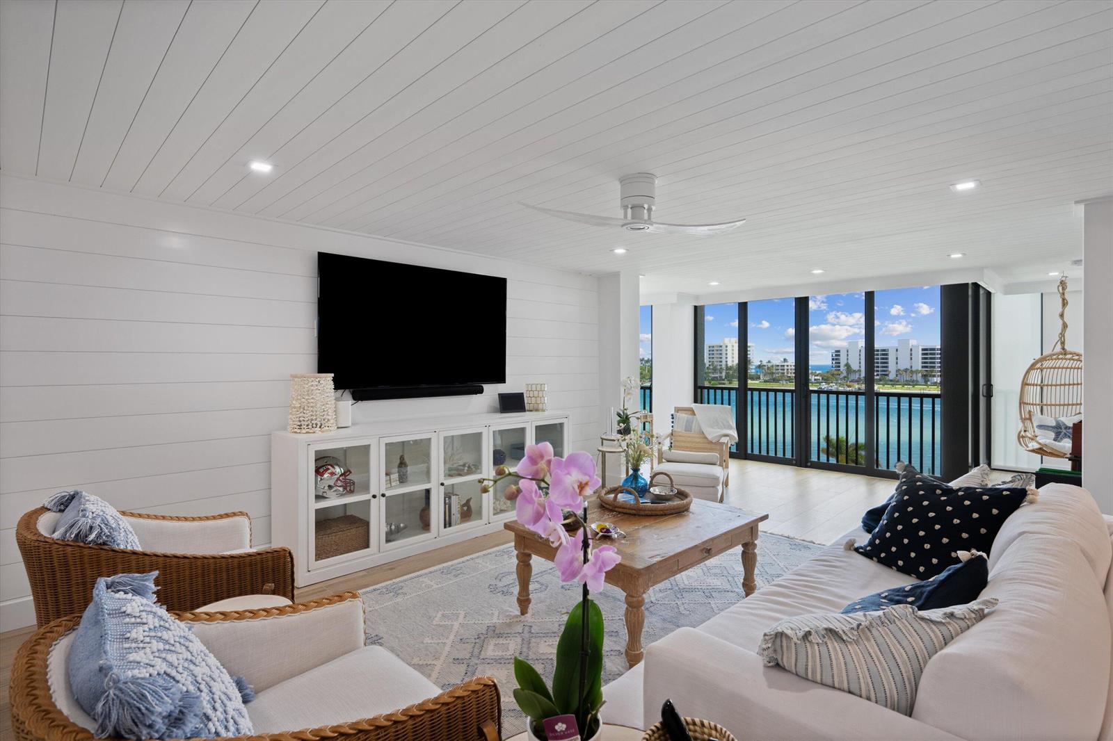 A bright living room features white shiplap walls, wicker chairs, and a view of water — 19800 S Sandpointe Bay Drive # 510, Tequesta FL 33469, TEQUESTA, FL