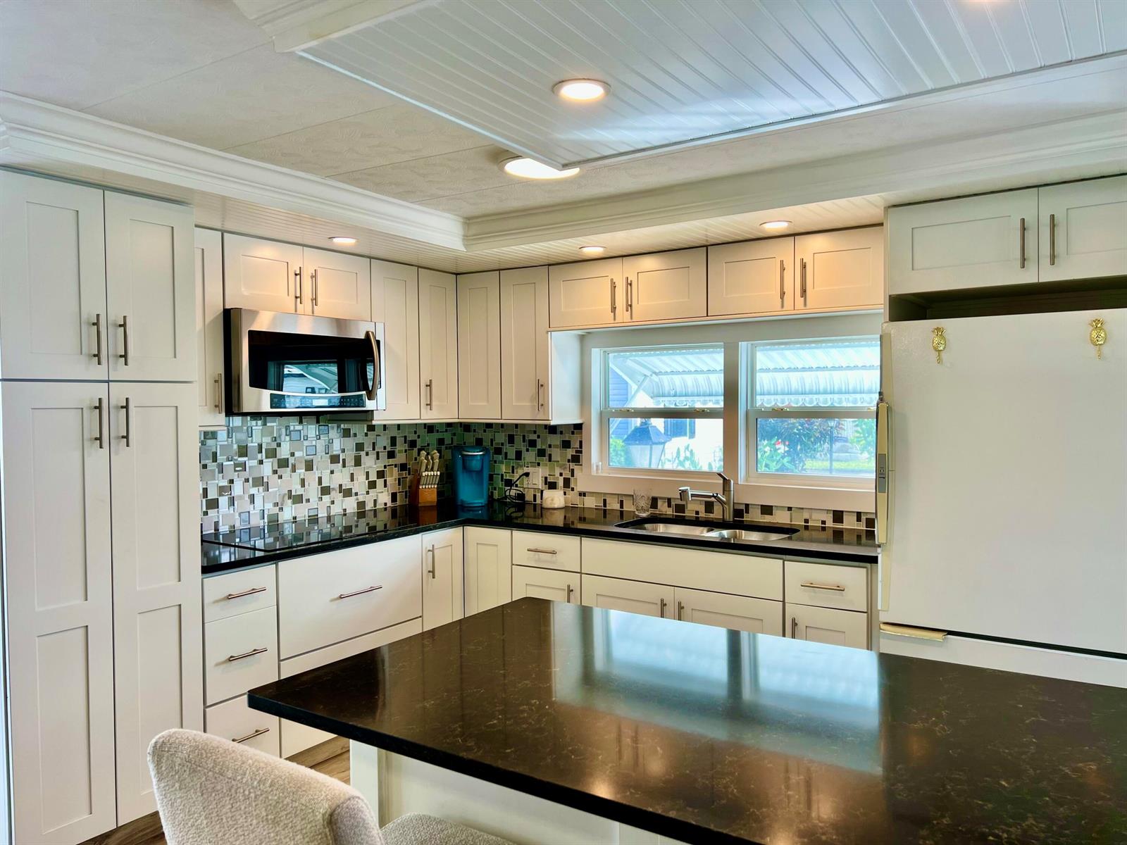 A kitchen with white cabinets, black countertops, a mosaic tile backsplash, and a center island — 1554 S 33rd Road, Hollywood FL 33021, HOLLYWOOD, FL