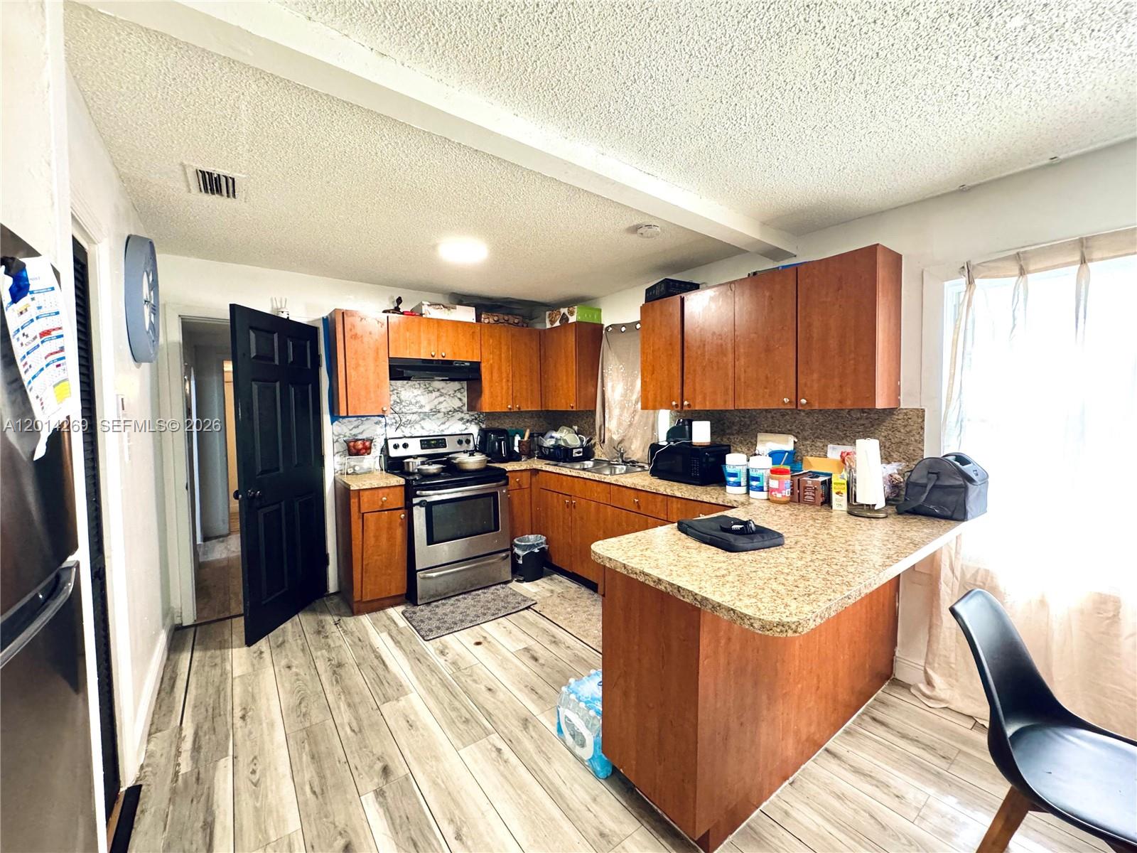 A kitchen features wood cabinets, granite-look countertops, stainless steel appliances, and wood-look flooring — 1484 NW 60th St, Miami FL 33142, MIAMI, FL