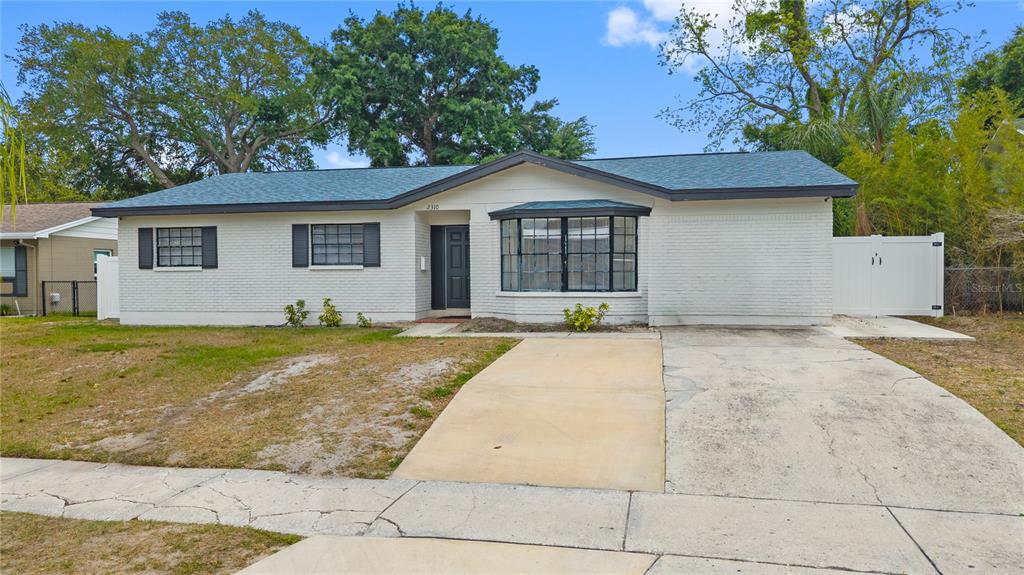 A single-story white brick house features a dark roof, a bay window, and a driveway — 2310 W KNOLLWOOD PLACE, TAMPA, FL