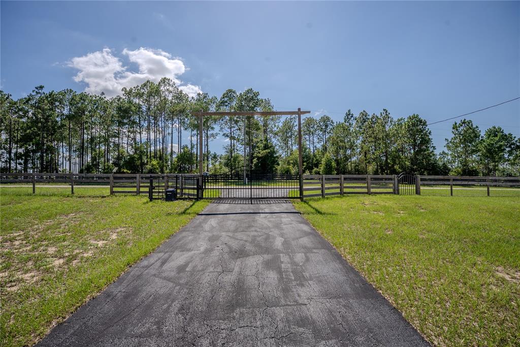 A paved driveway leads to a gated entrance with a wooden archway and fence — 13011 HIDDEN RIDGE LANE, CLERMONT, FL