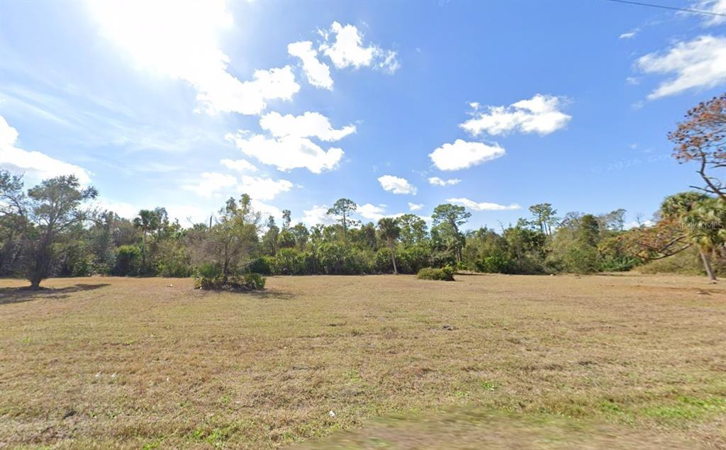 A large, flat, grassy vacant lot is surrounded by a dense line of trees — 24581 YACHT CLUB BOULEVARD, PUNTA GORDA, FL