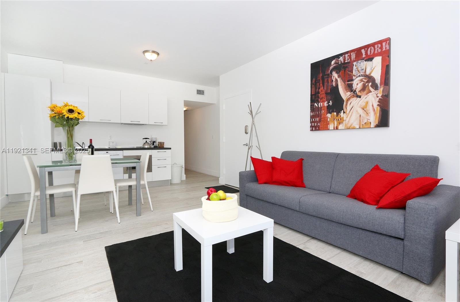 A modern living room and kitchen area features white cabinetry, a grey sofa, and artwork — 811 Jefferson Ave # 105, Miami Beach FL 33139, MIAMI BEACH, FL