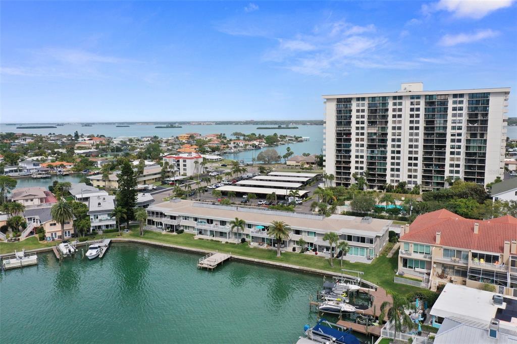 An aerial view shows a waterfront apartment complex with boat docks and a high-rise building — 400 LARBOARD WAY UNIT 103, CLEARWATER BEACH, FL