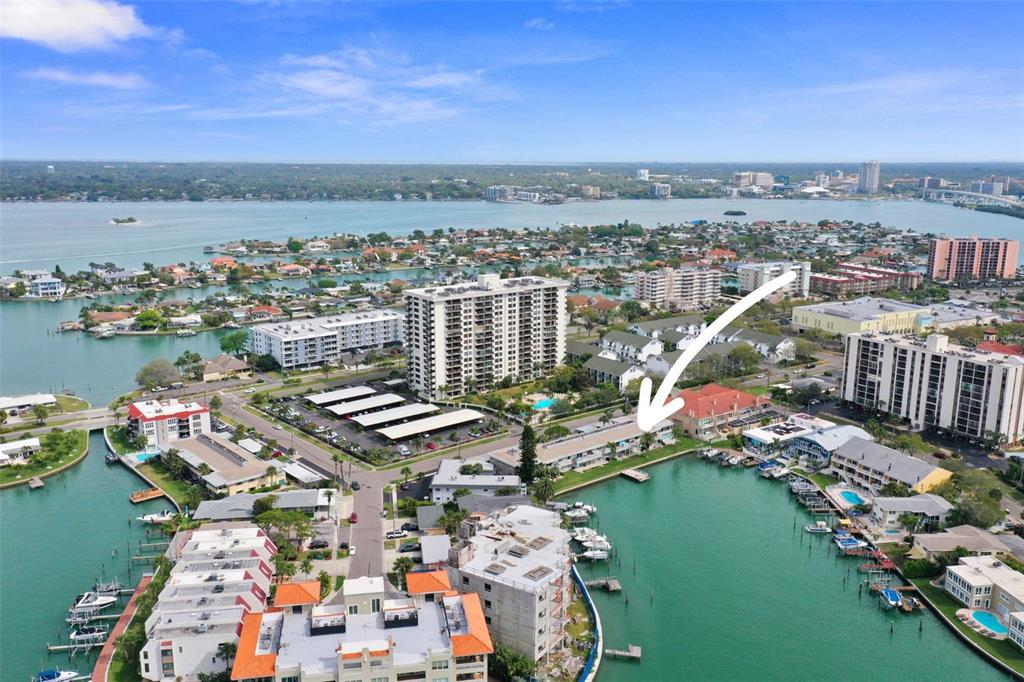 An aerial view shows a waterfront residential complex with boat slips and nearby high-rise buildings — 400 LARBOARD WAY UNIT 103, CLEARWATER BEACH, FL