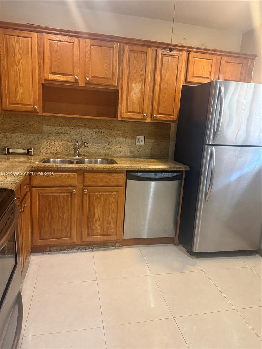 A kitchen features wood cabinets, granite countertops, a stainless steel dishwasher, and a refrigerator — 100 Ashbury Rd # 104, Hollywood FL 33024, HOLLYWOOD, FL
