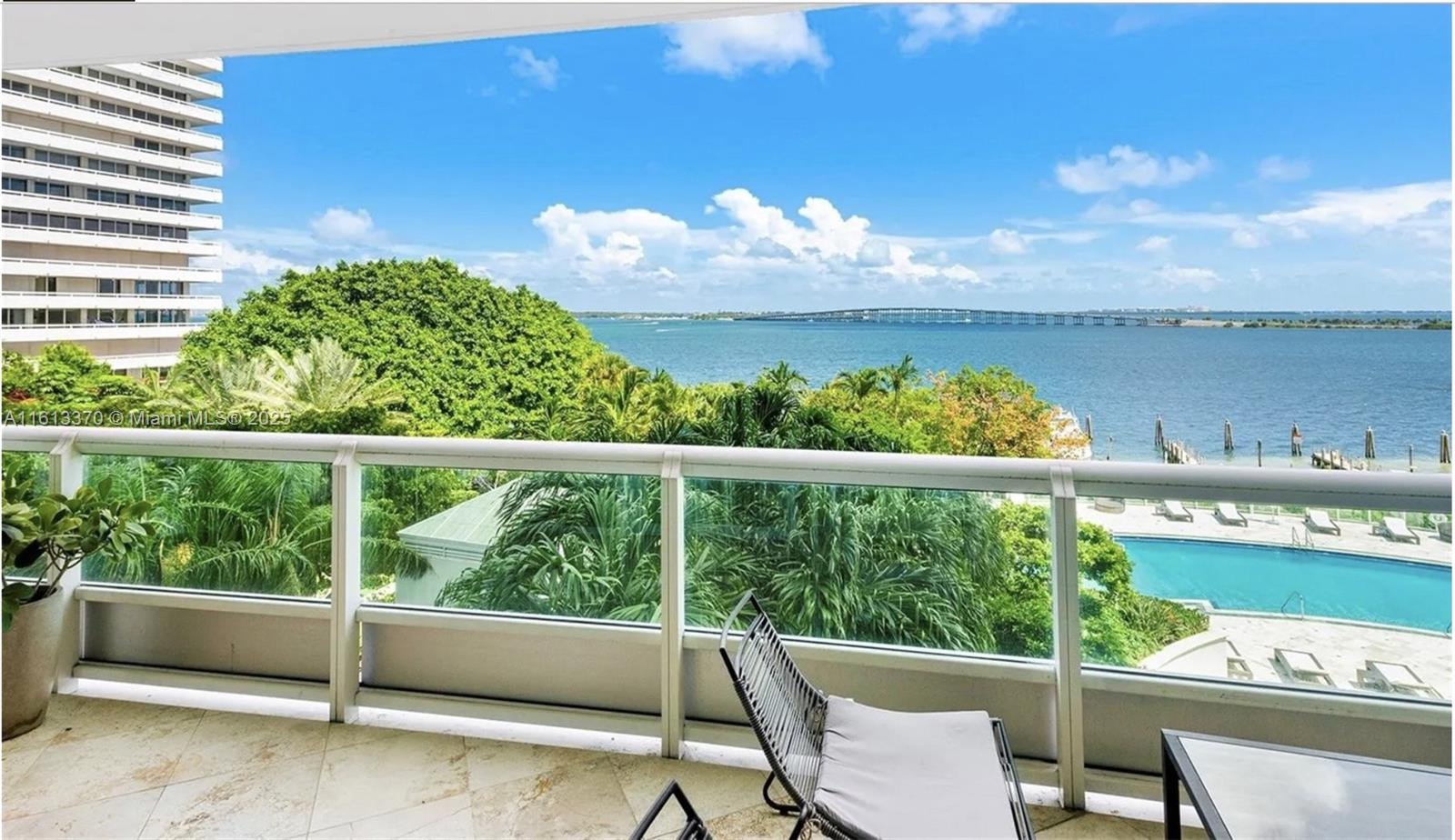 A balcony with a glass railing overlooks a swimming pool, lush trees, and the ocean — 1643 Brickell Ave # 704, Miami FL 33129, MIAMI, FL
