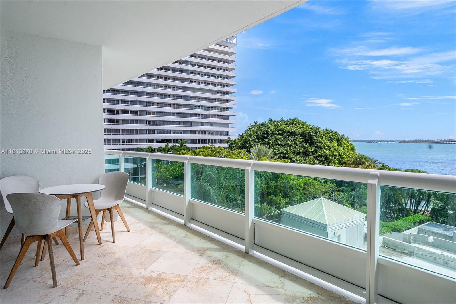 A balcony with a small table and chairs overlooks a large building and the ocean — 1643 Brickell Ave # 704, Miami FL 33129, MIAMI, FL