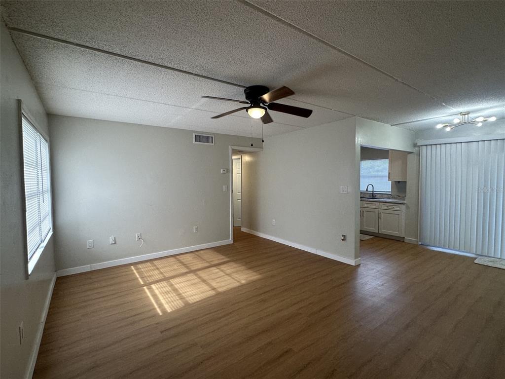 An empty living room with light wood-look flooring, a ceiling fan, and an adjacent kitchen — 1912 HONOUR ROAD UNIT 1, ORLANDO, FL