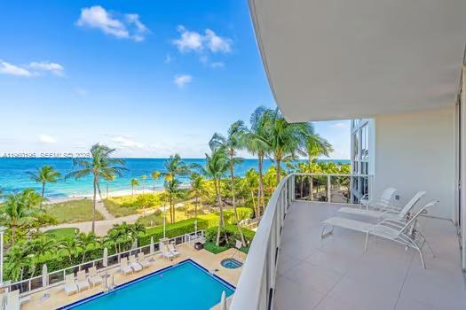 A balcony overlooks a swimming pool, palm trees, and the ocean under a blue sky — 10225 Collins Ave # 304, Bal Harbour FL 33154, BAL HARBOUR, FL