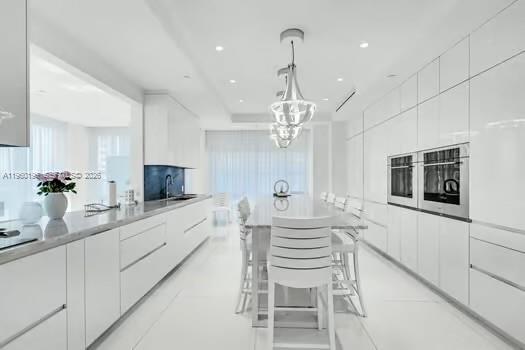 A modern, all-white kitchen features high-gloss cabinetry, a central island with bar seating, and pendant lighting — 10225 Collins Ave # 304, Bal Harbour FL 33154, BAL HARBOUR, FL