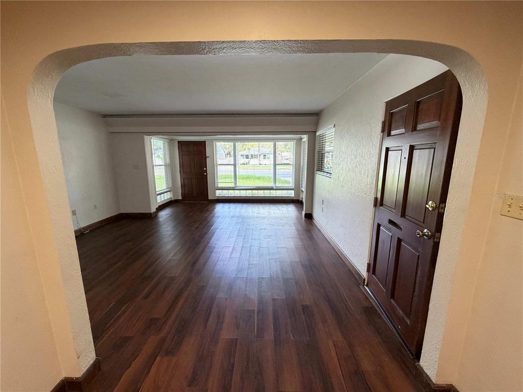 An empty living room features dark wood-look flooring, an arched entryway, and a large window — 3215 N ORANGE AVENUE, ORLANDO, FL