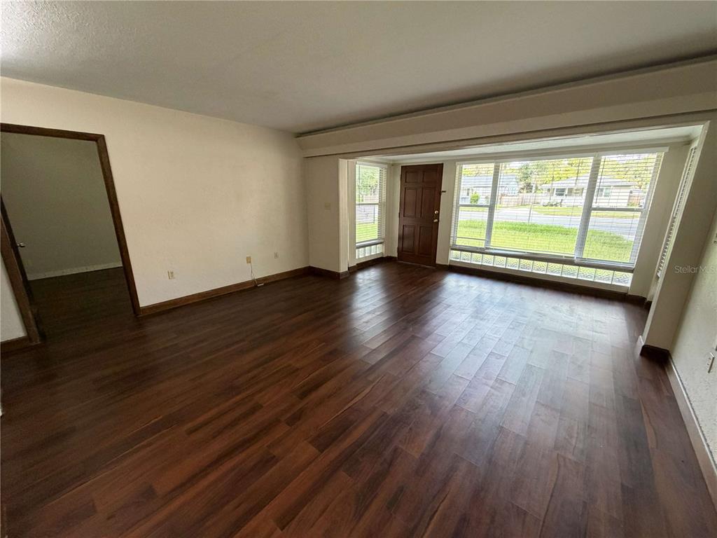 An empty living room features dark wood-look flooring, white walls, and a large front window — 3215 N ORANGE AVENUE, ORLANDO, FL