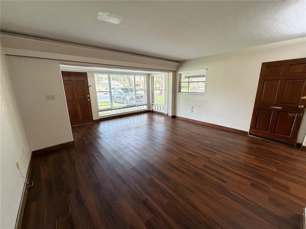 An empty room with dark wood-look flooring, two wooden doors, and a large front window — 3215 N ORANGE AVENUE, ORLANDO, FL