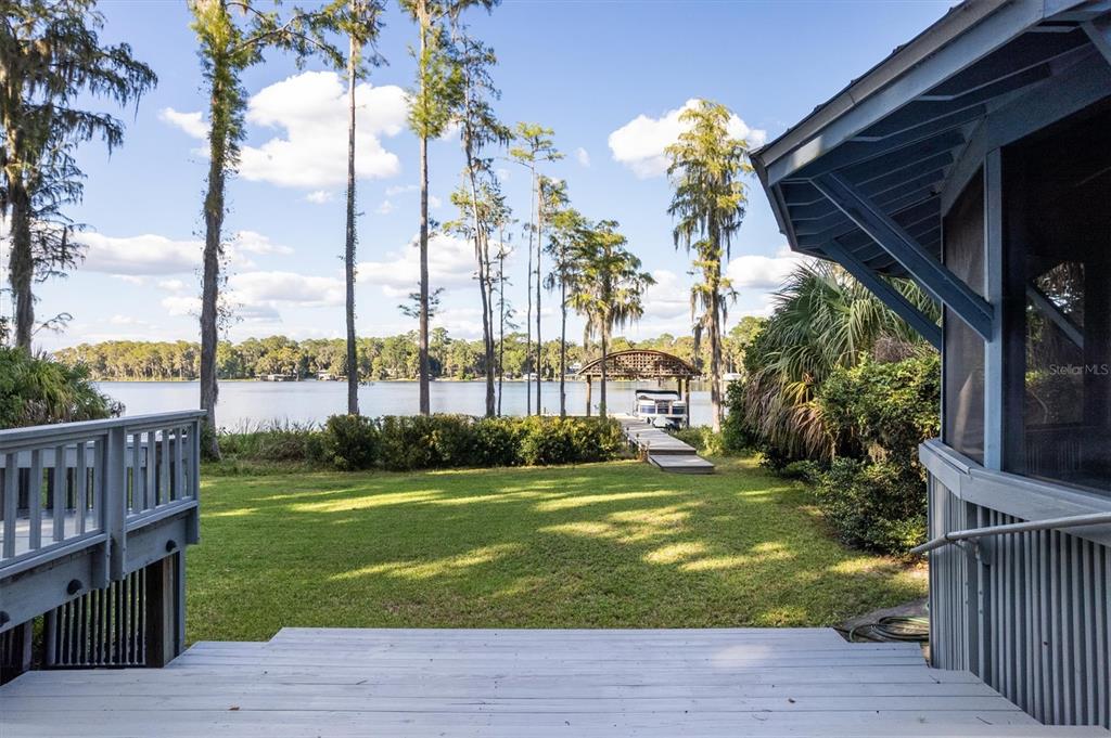 A wooden deck overlooks a grassy backyard leading to a lake with a boat dock — 25608 DEVONIA STREET, MELROSE, FL