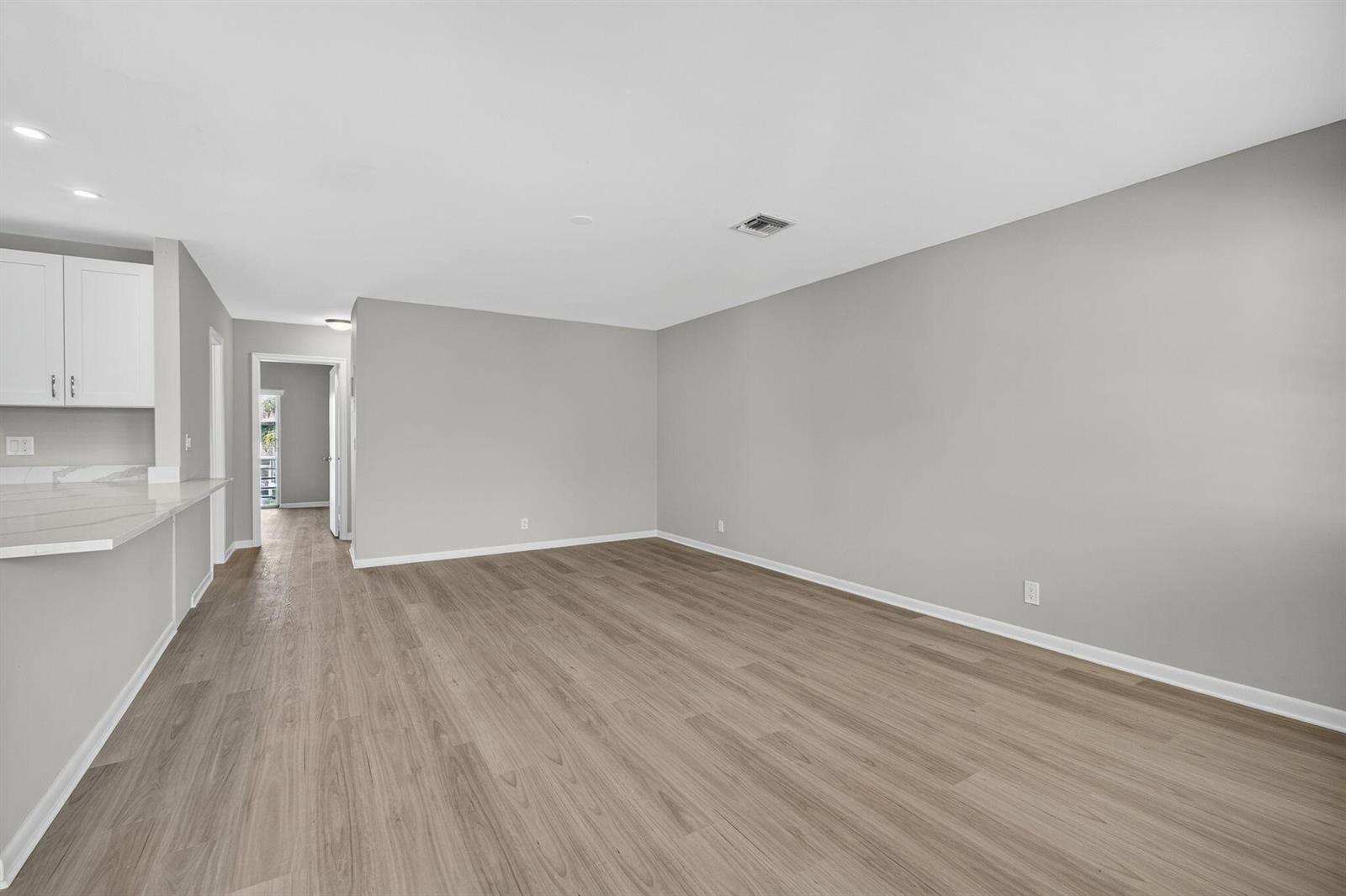 An empty living room features light gray walls, wood-look flooring, and an adjacent kitchen counter — 42 Easthampton B, West Palm Beach FL 33417, WEST PALM BEACH, FL