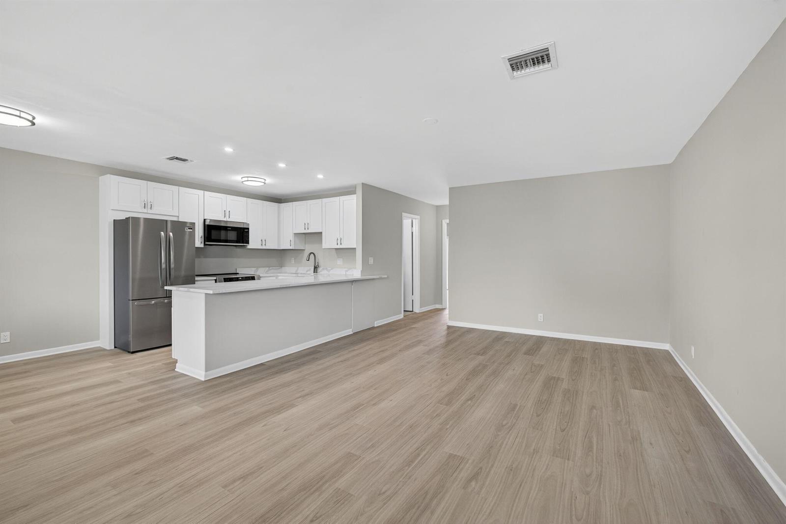 A kitchen with white cabinets and stainless steel appliances opens to a spacious living area — 42 Easthampton B, West Palm Beach FL 33417, WEST PALM BEACH, FL