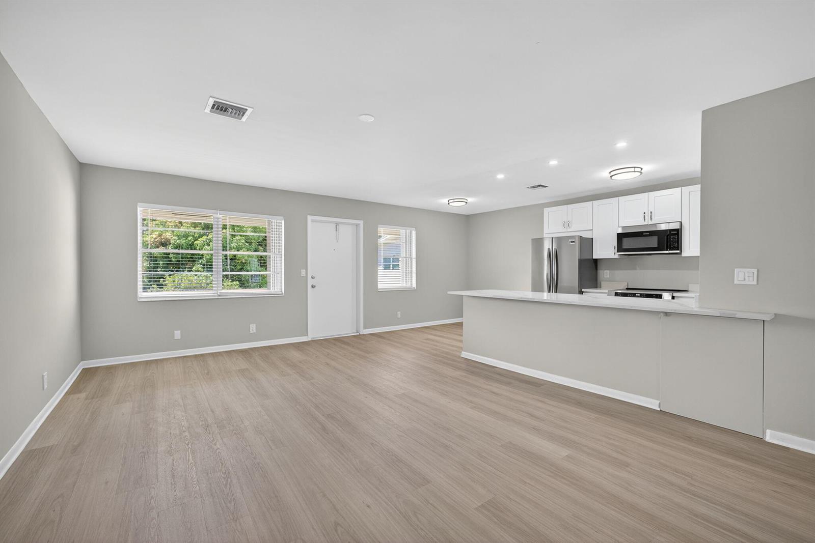 A bright, open-concept living area features light wood-look flooring, gray walls, and a modern kitchen — 42 Easthampton B, West Palm Beach FL 33417, WEST PALM BEACH, FL