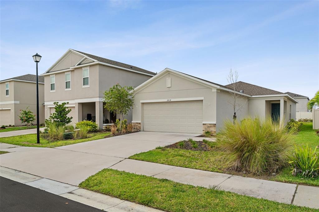 A tan single-story house with a two-car garage sits next to a two-story home — 6434 MILESTONE LOOP, PALMETTO, FL